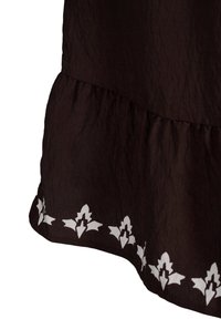 Svart tygklänning med ett lager på neder kanten och ett vitt blommönster längs den nedre kanten. Texturen ser krinklad ut.