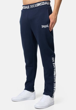 Navy blue sweatpants with an elastic waistband, side pockets, and a white logo print. Features contrasting brand accents along the legs.