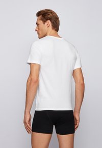 Witte katoenen t-shirt met korte mouwen, ronde halslijn, eenvoudige design, gedragen met zwarte shorts, van achteren weergegeven.