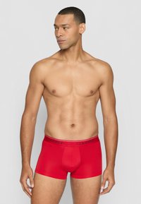 Rote Boxer-Shorts aus einem weichen, elastischen Stoff mit einem schwarzen Calvin Klein-Logo-Bund. Saubere Nähte und glatte Textur sind deutlich sichtbar.