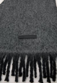 Sötétszürke, textúrált sál hosszú fekete bojtokkal, a közepén fekete címkével, amelyen a következő felirat olvasható: "CLASSIC. MODERN. YOURS."