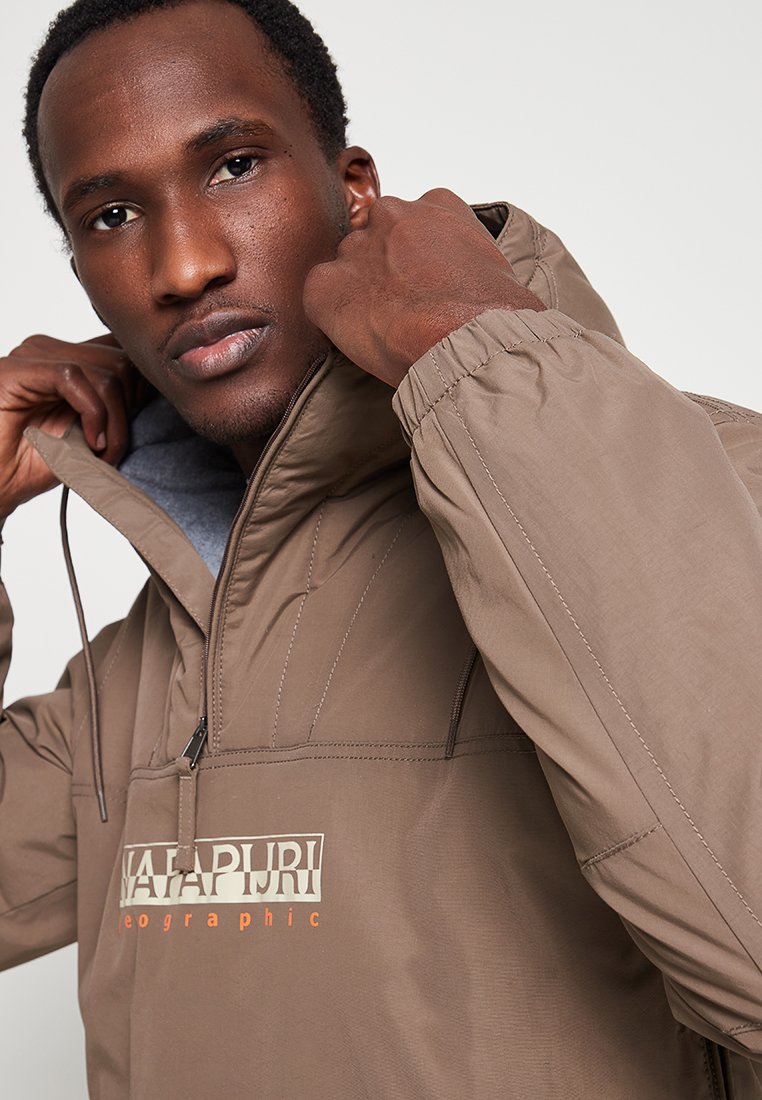 Chaqueta marrón de pulóver con cierre zip, puños elásticos y detalle de logo. Presenta una textura de tela suave y capucha ajustable.