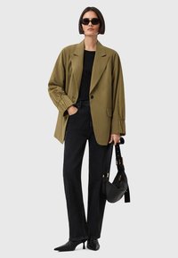 Blazer verde oliva con una vestibilità rilassata, top nero, jeans scuri, scarpe nere con punta e borsa nera con tracolla.