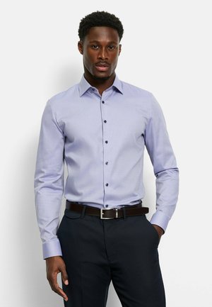 Light purple button-up shirt with a subtle check pattern, long sleeves, dark buttons, and a collar, paired with dark trousers and a brown belt.