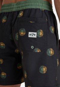 Pantaloni da bagno neri con una vita elastica verde, caratterizzati da un motivo di design circolari in giallo e verde. Include una tasca sul retro con pattina.