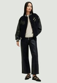 Μαύρο varsity μπουφάν με κεντημένα στοιχεία, συνδυασμένο με ψηλόμεσα δερμάτινα παντελόνια και μαύρες επίπεδες φούστες. Λείο ύφασμα, χαλαρή εφαρμογή.