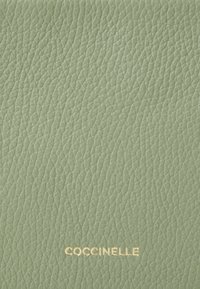 Pelle verde texturizzata con un sottile motivo a grana, con un logo dorato "Coccinelle" nella parte inferiore.