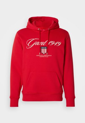 Sweatshirt vermelho com capuz, bolso frontal, cordões e texto branco "Gant 1949" acima de um emblema em forma de escudo com estrelas e listras.