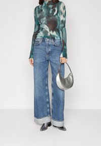 Long-sleeve, teal and black patterned top with ribbed texture; paired with wide-leg, light blue denim jeans and a silver handbag.