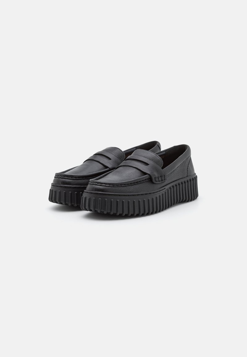 Mocassins en cuir noir avec deux brides surélevées, semelles épaisses à motifs et texture lisse. Le design présente un bout rond et des côtés bas.