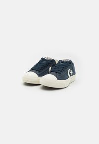 Zapatillas de ante azul con puntera y suela de goma blanca. Cintas en azul a juego; la etiqueta de la marca en la lengüeta dice "ALL STAR". Diseño clásico de corte bajo.