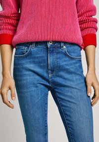 Červeno-růžový žebrovaný svetr v kombinaci s modrými denimovými džínami. Svetr má volný střih, zatímco džíny mají štíhlou siluetu a pět kapes.