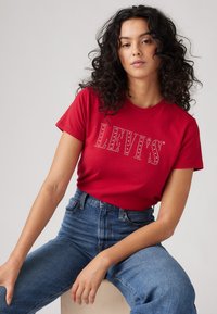 Punane puuvillane T-särk lühikeste varrukatega, mille esiküljel on kividest kaunistatud "LEVI'S" logo. Kombineeritud kõrge vöökohaga siniste teksadega.