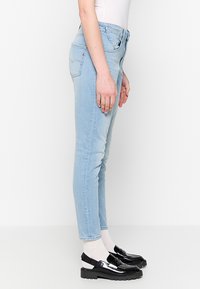 Lichtblauwe denim jeans met een slim fit, vijf-vakken ontwerp en subtiele vervaging. Gepaard met zwarte loafers en witte enkelsokken.