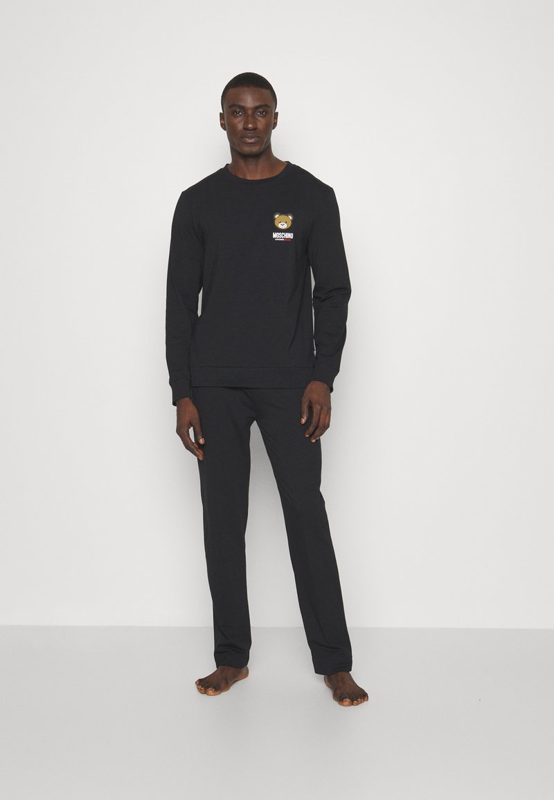 Black loungewear set featuring long-sleeve top with bear graphic and logo, matching pants, made from soft fabric, plain design.