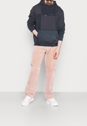 Marineblauwe hoodie met een gestructureerd patchworkontwerp, gecombineerd met lichtroze corduroybroeken en witte sneakers. Minimalistische stijl, comfortabele pasvorm.