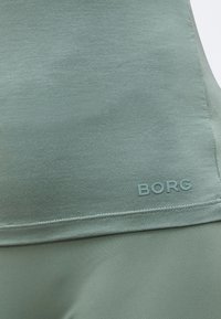 Κοντινό πλάνο πράσινου αθλητικού υφάσματος με ραμμένο τελείωμα και το κείμενο "BORG" τυπωμένο κοντά στο κάτω άκρο.