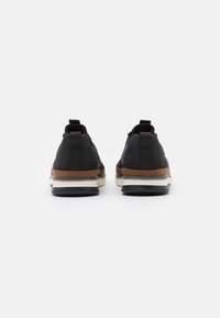 Black athletic shoes with a brown leather accent at the midsole, featuring a textured fabric upper and rear pull tabs for easy wear.