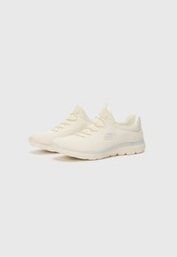 Light beige athletic shoes made of textured mesh material, featuring a cushioned sole and subtle logo on the side. Laces in matching color.