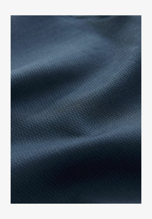 Close-up van donkerblauwe stof met een fijne geweven textuur en subtiele licht- en schaduweffecten die zachte plooien creëren.