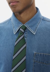 Denim srajca s ostrim ovratnikom, ki ima žep na prsih. Zelen kravata z diagonalnimi črtami v sivi in mornarski modri barvi dopolnjuje obleko.