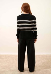 Czarny sweter prążkowany z poziomymi białymi paskami w górnej części. Połączony z szerokimi czarnymi spodniami. Prosty design, bez widocznych logotypów.