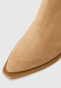 Botine ancle din suede de culoare bej, cu vârful ascuțit, textură netedă și o talpă subțire, solidă, de culoare bej. Design elegant și aerodinamic.