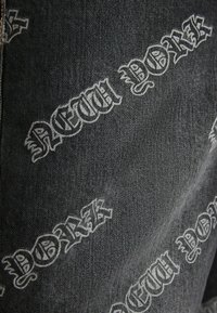 Svart denimtyg med ett upprepat vitt grafiskt tryck av "NEW YORK" i stiliserad font, vilket skapar ett djärvt och strukturerat mönster.