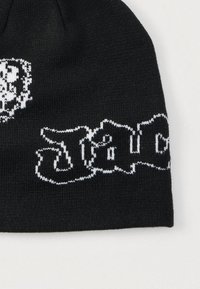 Μαύρο πλεκτό σκουφάκι με λευκά γράμματα και διακοσμητικό σχέδιο. Η υφή είναι λεία με στενή εφαρμογή και ριμπ σχέδιο στη άκρη.