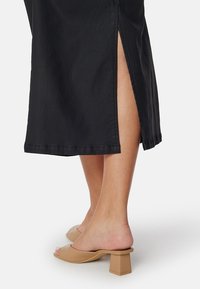 Zwarte midi-rok met een zij-split en netjes afgewerkte zoom. Gemaakt met beige blokhakken, die een soepele textuur en een minimalistisch ontwerp laten zien.