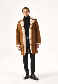 Palton din shearling maro cu o căptușeală din blană ecologică albă, având un sistem de închidere cu nasturi în față, guler lat și buzunare laterale. Purta peste pantaloni negri și cizme.