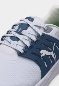 Λευκό αθλητικό παπούτσι με μπλε πλαστικό πλαϊνό κλουβί με το λογότυπο Puma, λευκά και γκρι κορδόνια με στίγματα και επάνω μέρος από πλεγμένο ύφασμα.