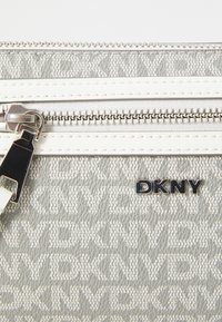 Clutch in tessuto grigio con logo DKNY, dotato di una zip argentata con un tirante nero e un motivo testurizzato di branding ripetuto. Dettagli bianchi.