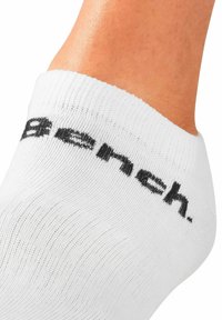 Weiße Knöchelsocke aus einem dünnen, strukturierten Stoff mit einem schwarzen "Bench."-Logo nahe dem Bund. Glatte Oberfläche mit gerippten Details.