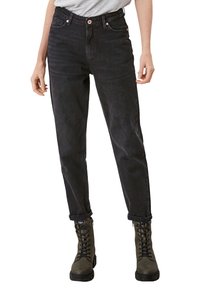 Czarne, wysokiego stanu jeansy o zwężanym kroju, z zamknięciem na guzik, przednimi kieszeniami i podwiniętymi nogawkami, w połączeniu z zielonymi butami na sznurowadła.