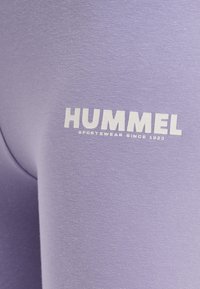 Paars sportkledingstof met witte tekst "HUMMEL SPORTSWEAR SINCE 1923" bedrukt op het oppervlak.
