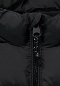 Veste rembourrée noire avec fermeture éclair dotée d'une tirette texturée, tissu lisse et design à col haut.