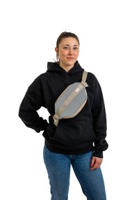 Borsa a tracolla in tessuto grigio indossata a croce, con una tracolla regolabile beige, texture liscia, forma ovale e un discreto dettaglio di branding.