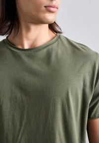 Olíva zöld pamut póló klasszikus kerek nyakkal és rövid ujjakkal, sima textúrával és minimalista dizájnnal.