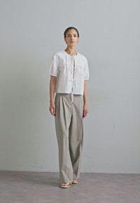 Blouse blanche à manches bouffantes courtes avec un nœud à l'avant et un pantalon large gris. Le tissu semble lisse, avec un design minimaliste et des couleurs neutres.