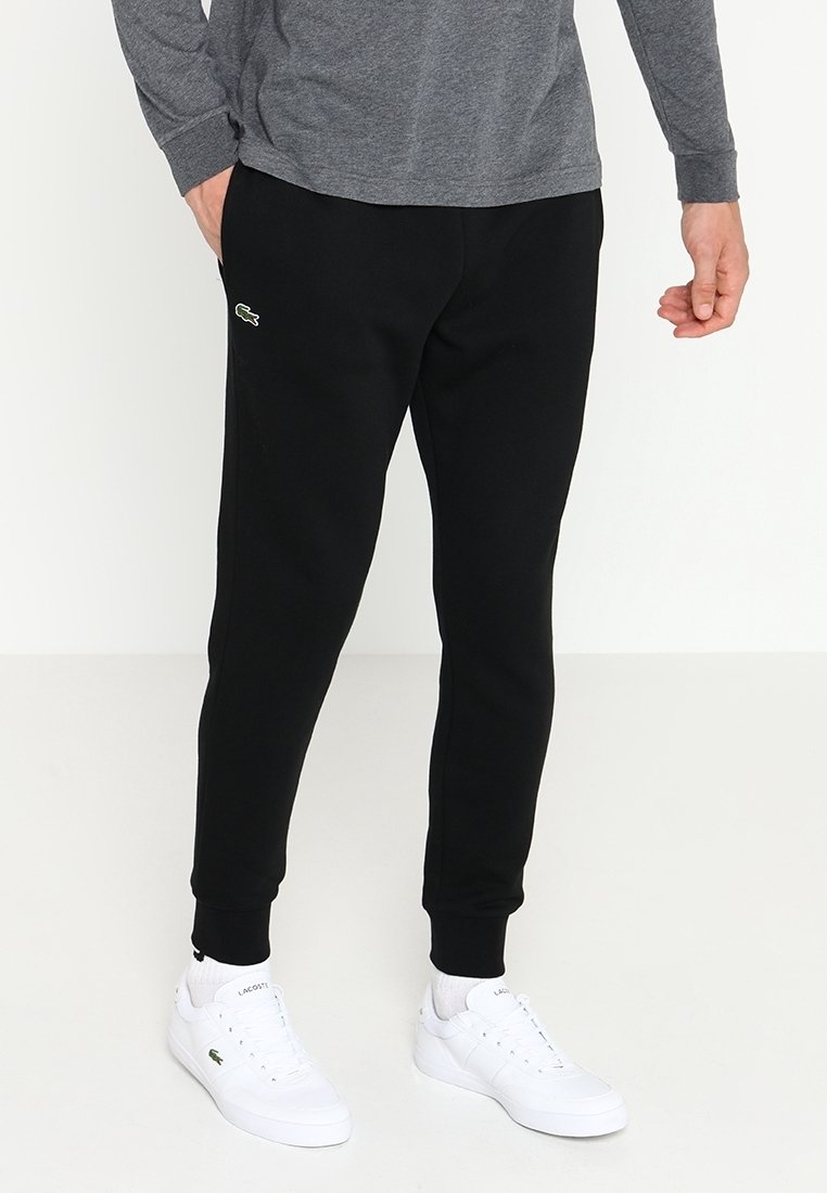 Joggers de algodón negros con puños elásticos, que presentan un logotipo sutil en el muslo. Combinados con zapatillas blancas, que complementan una camiseta de manga larga gris.