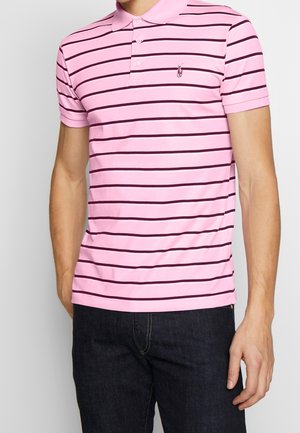 Różowa koszulka polo w paski z ciemnofioletowymi poziomymi liniami, z krótkimi rękawami i kołnierzykiem. Posiada małe logo na piersi.