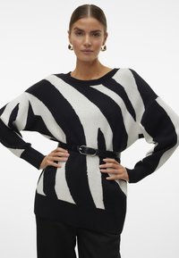 Maglione a righe bianche e nere con scollatura ampia e maniche lunghe, abbinato a una cintura nera. Tessuto morbido e vestibilità rilassata.
