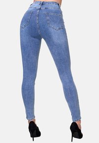 Jeans ajustados de denim azul claro. Presentan una cintura alta, dos bolsillos traseros y una silueta ceñida. Llevados con tacones negros.