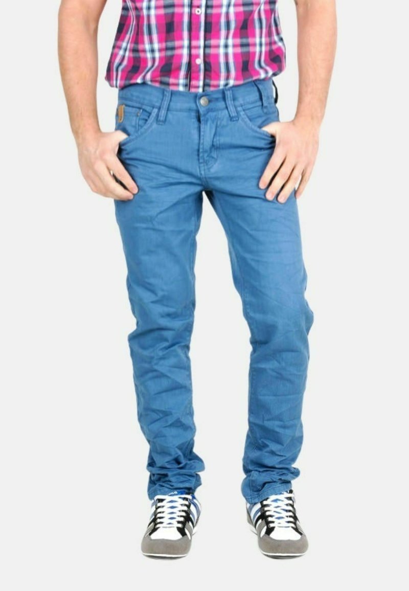 Vaqueros de mezclilla azul con un corte ajustado, que presentan un sutil detalle texturizado y un diseño clásico de cinco bolsillos. Combinados con zapatillas negras y blancas.