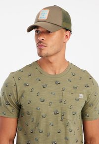 Olive green T-shirt with small surf-themed patterns, featuring a pocket and short sleeves. Matching olive cap with mesh back and logo patch.