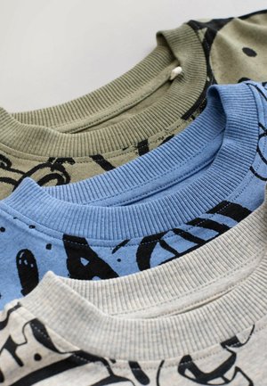 Tre felpe girocollo piegate nei colori beige, blu e verde oliva con scritte grafiche nere su una superficie uniforme.