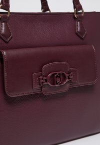 Borsa in pelle bordeaux con forma strutturata, superficie testurizzata, dettagli in metallo dorato e chiusura a gancio.