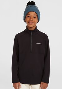 Zwarte zip-hals trui met lange mouwen en details op de bovenste borstnaad. Draagt een blauwe gebreide muts met een pompon.