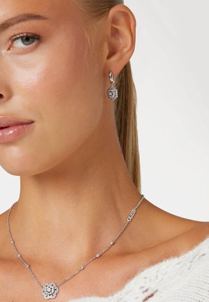 Zilveren oorbellen met een geometrisch ontwerp en een sprankelende afwerking. Vergezeld van een bijpassende ketting met een bloemenhanger.